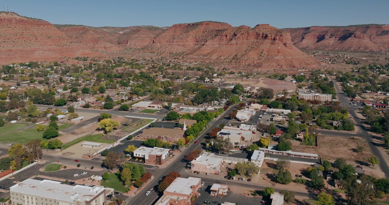 Vista aerea dei quartieri e delle strade di Kanab, Utah, con scogliere desertiche rosse che si ergono dietro la città, sfondo immobiliare da drone.