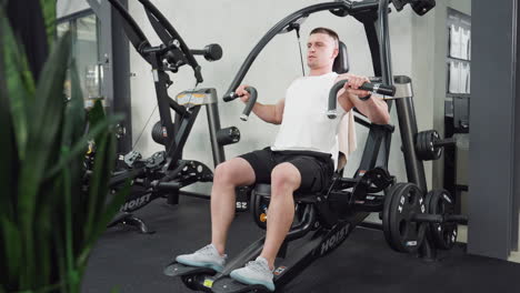 fitness enthusiast works out on weight machine doing chest press, expressing intense energy and strength on his face, muscles flexing under bright gym lighting, flower vase visible in corner