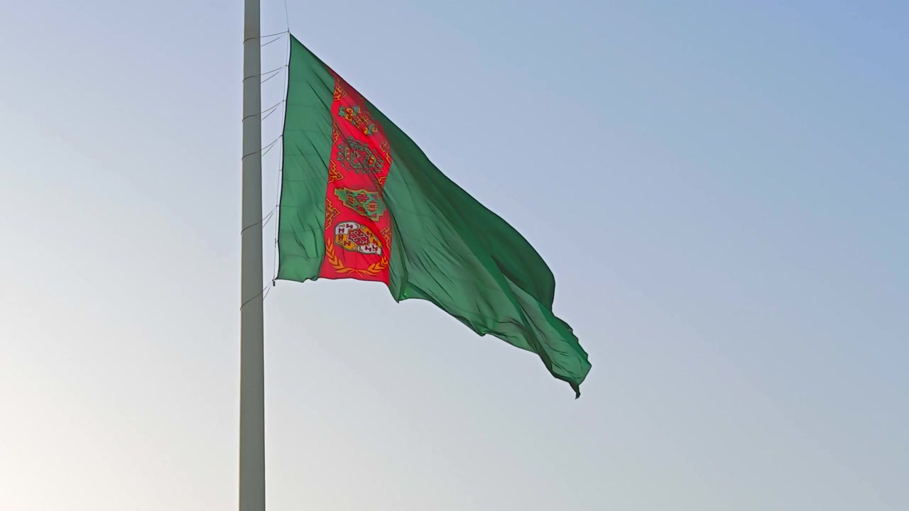 Bandera nacional de Turkmenistán ondeando contra un cielo azul claro.