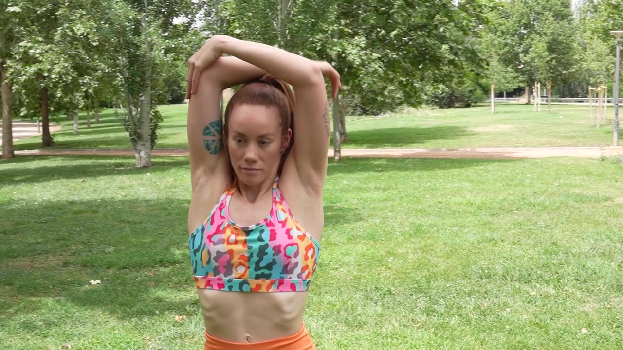 Uma mulher faz alongamentos de ombro em um parque, focando na saúde e flexibilidade em seu treino.