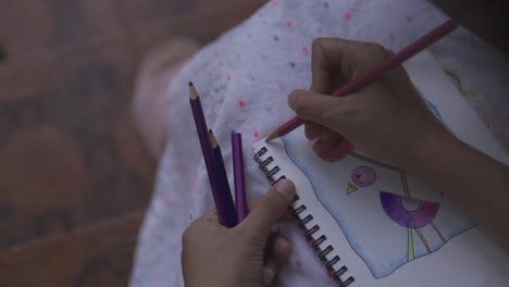 vídeo de cerca de una estudiante vestida con un vestido blanco dibuja con lápiz de color en el papel, sosteniendo lápices en la otra mano