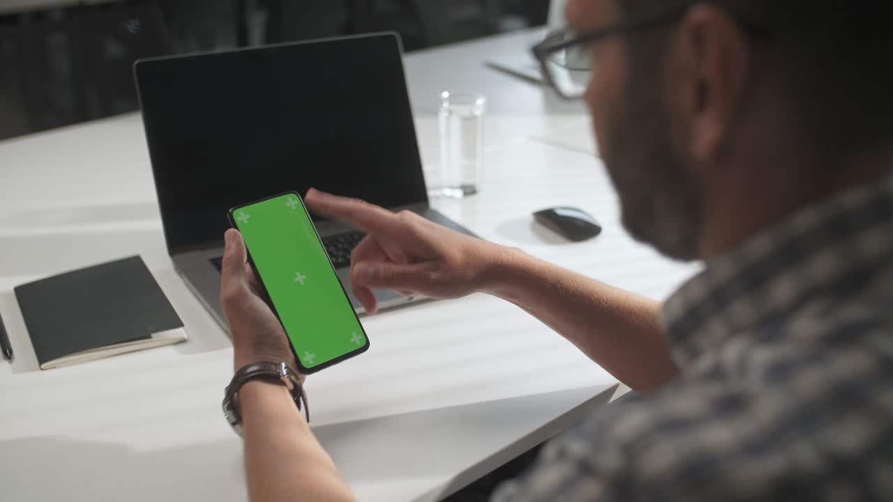 sobre el hombro de un hombre de negocios trabajando en el interior de la oficina en el teléfono, mirando la pantalla verde