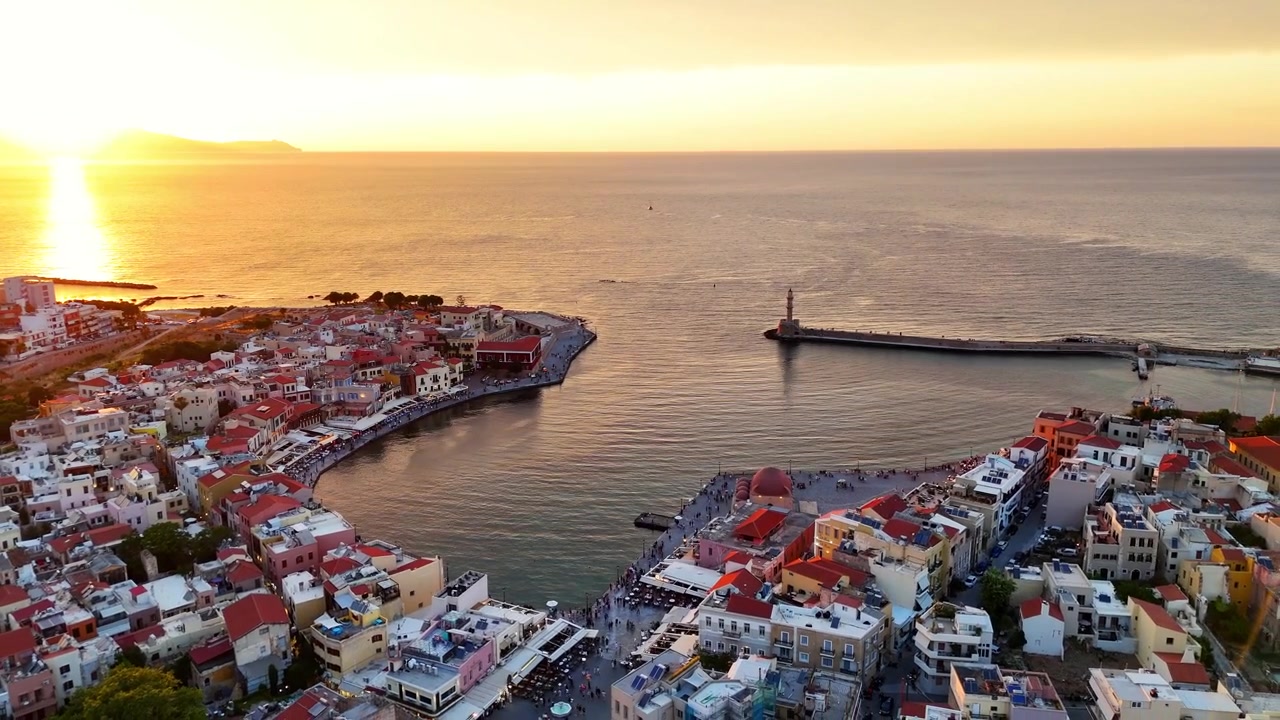 Il Vecchio Porto Veneziano di Chania circonda il Faro Egiziano e il lungomare storico a Chania, Creta, Grecia, con la diga foranea che si estende nel Mar di Creta durante una ripresa aerea con drone in allontanamento.