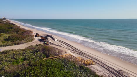 4K-Luftaufnahme-Von-Baggern-Und-Muldenkippern,-Die-Den-Strand-In-Der-Nähe-Tropischer-Vegetation-Und-Des-Blauen-Ozeans-Räumen