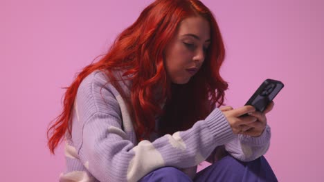 Studio-Shot-Of-Young-Gen-Z-Woman-Gaming-Streaming-Or-Using-Social-Media-On-Mobile-Phone-Against-Pink-Background