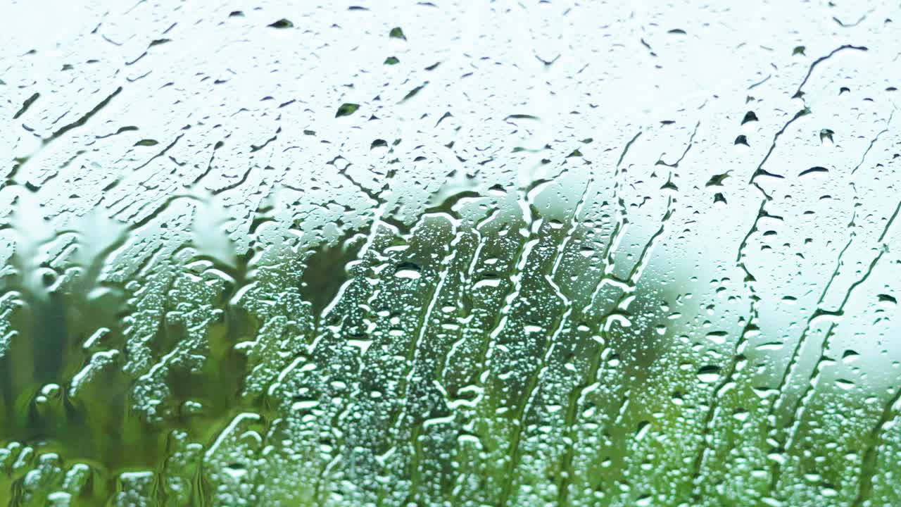Raindrops trickle down glass, blurring scenic view