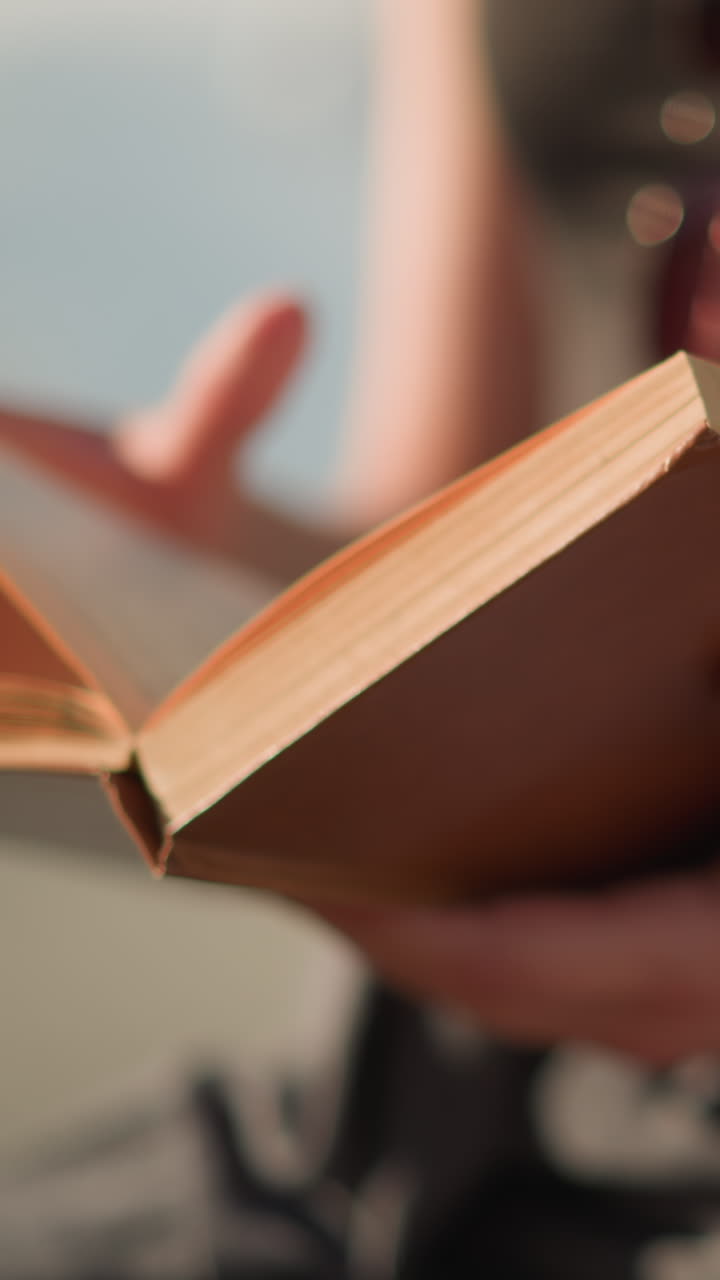 primer plano de un individuo sosteniendo y volteando suavemente las páginas de un libro a medida que se mueven hacia la derecha debido al viento, el individuo está ligeramente borroso igual que el fondo, con un suave resplandor de luz solar
