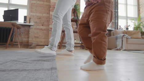 legs of mother and toddler walking in living room