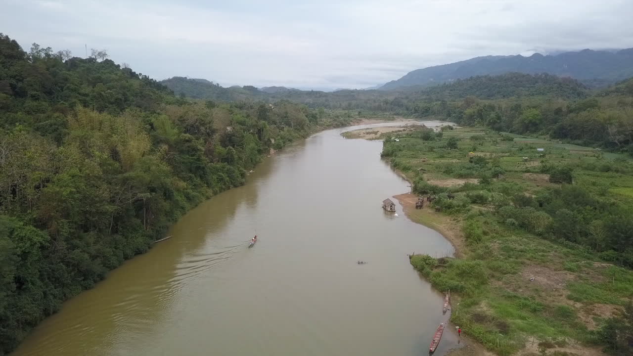 Ripresa aerea che scende verso una piccola imbarcazione che naviga un fiume nella fitta giungla del Laos