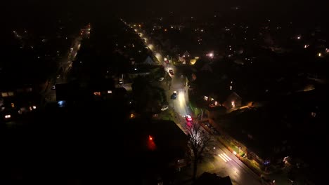 Cars on main street of housing area with single family homes at night. Foggy and rainy midnight in American city. Aerial wide shot.