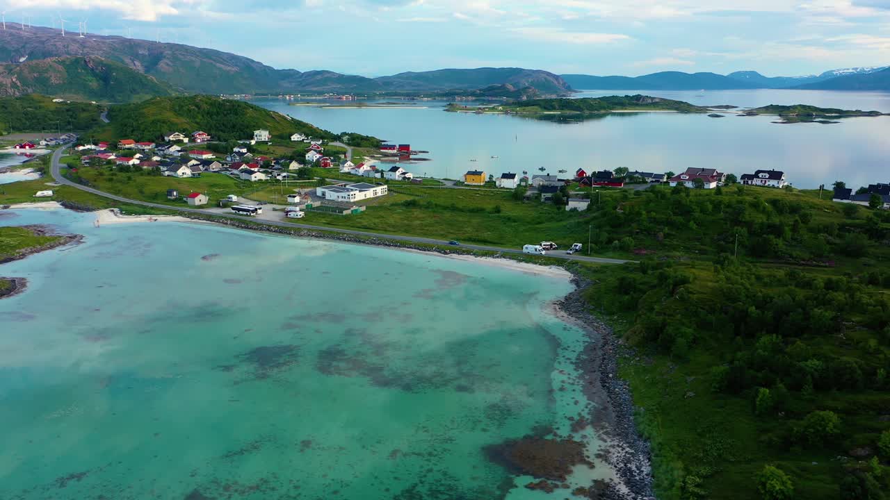 Drone shot following a caravan driving at the turquoise ocean, on the coast of the Arctic sea, in the town of Sommaroya islands, summer evening, in Troms, Norway - tracking, aerial view