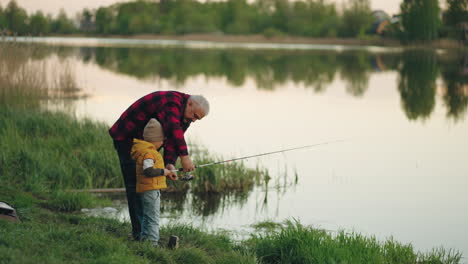 feliz abuelo y pequeño nieto están pescando juntos en la mañana de verano de pie en la hermosa orilla del lago