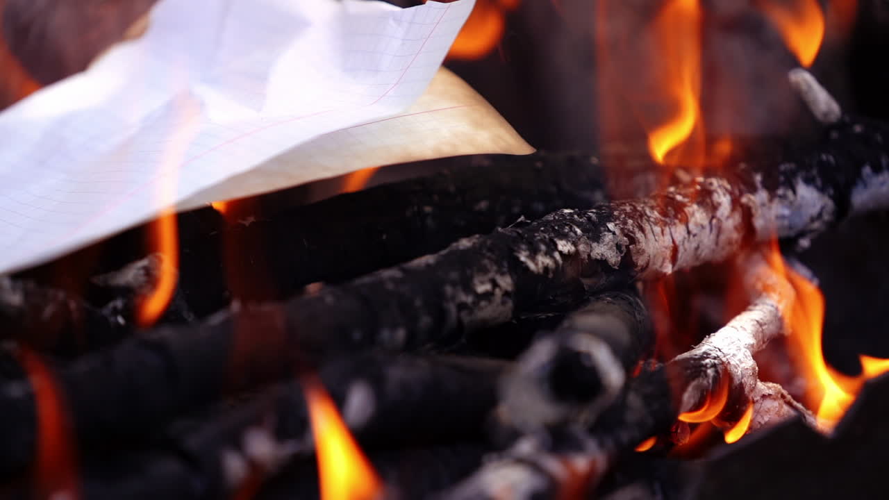 Detailed fire. White paper falling into the fire and began to burn. Smoldered logs in vivid flame. Close-up. Slow motion.