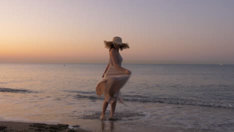 happy healthy romantic woman circling around on the beach wearing dress and straw hat