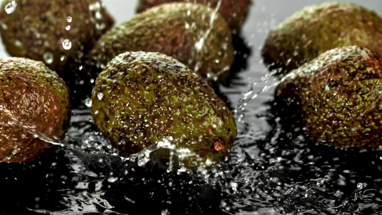 Acqua che schizza su avocado freschi e verdi in slow motion