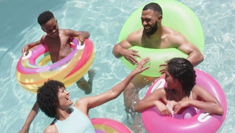 felices padres afroamericanos, hijo e hija flotando en inflables en una piscina soleada, en cámara lenta