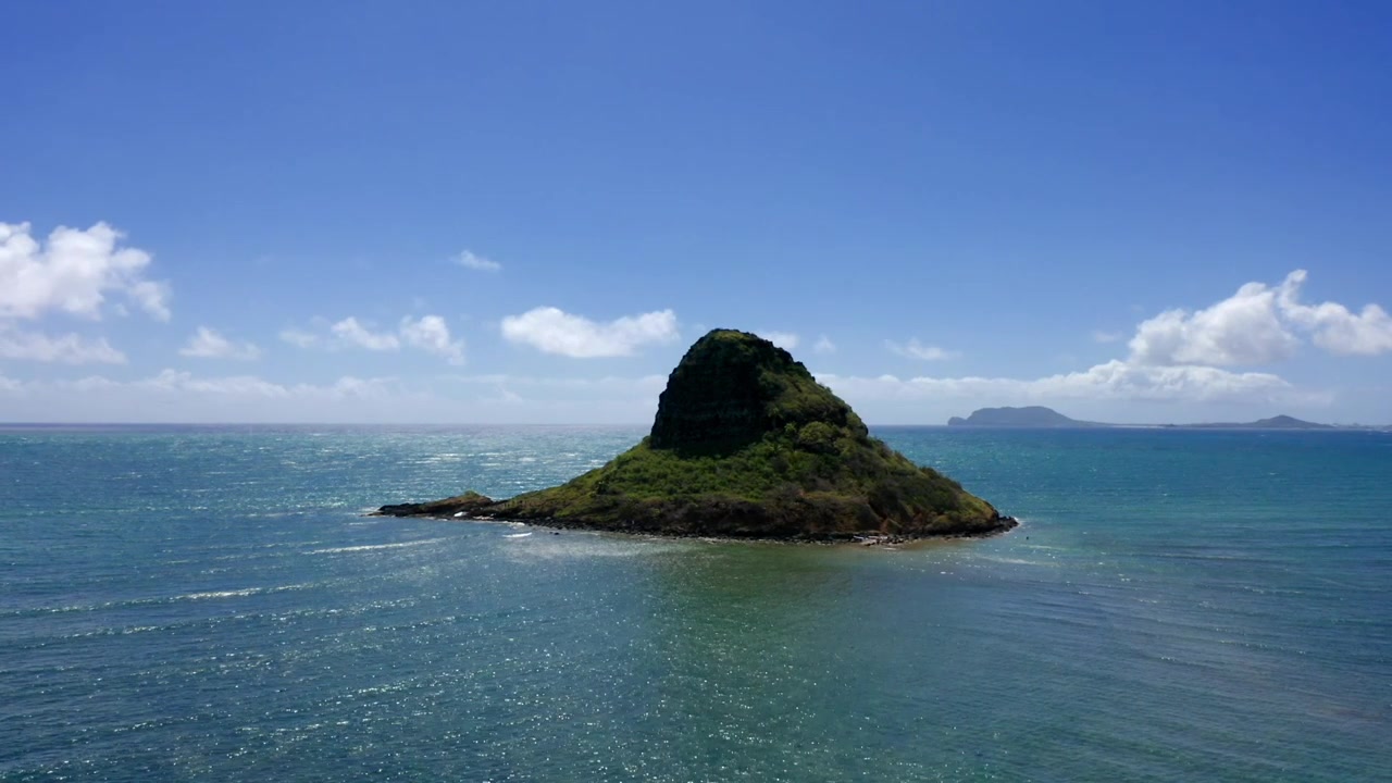 Luftaufnahme, die um Mokolii oder Chinaman's Hat inmitten wunderschöner offener Ozeangewässer unter blauem Himmel an der Luvseite von Oahu schwenkt