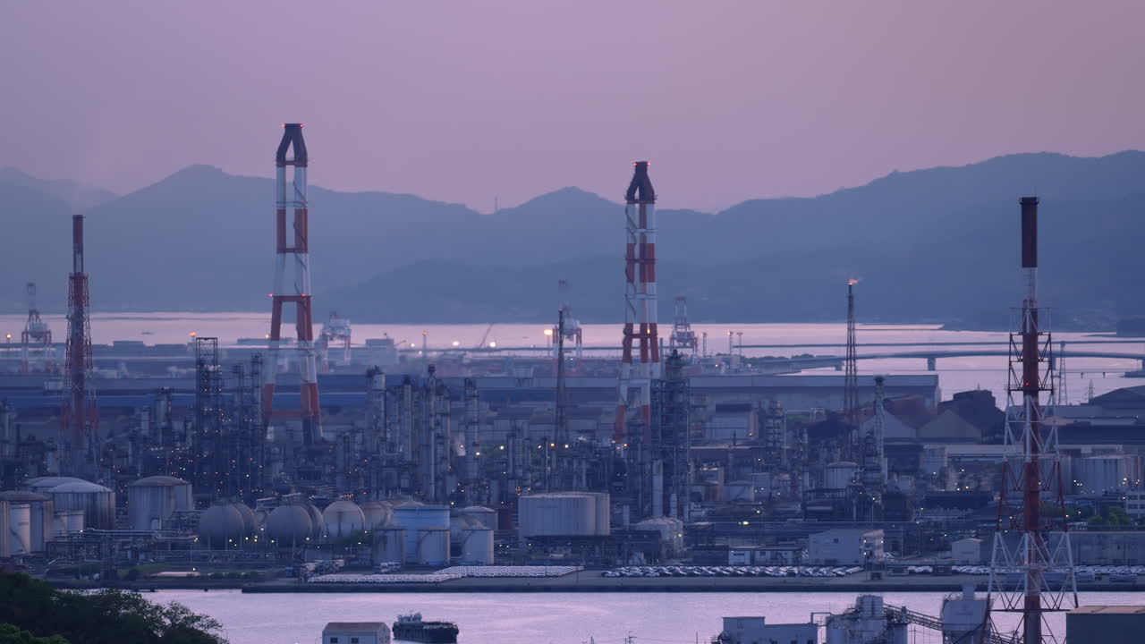 黃昏時分，一座龐大的工業廠房，煙囪冒著煙，火炬塔熊熊燃燒。