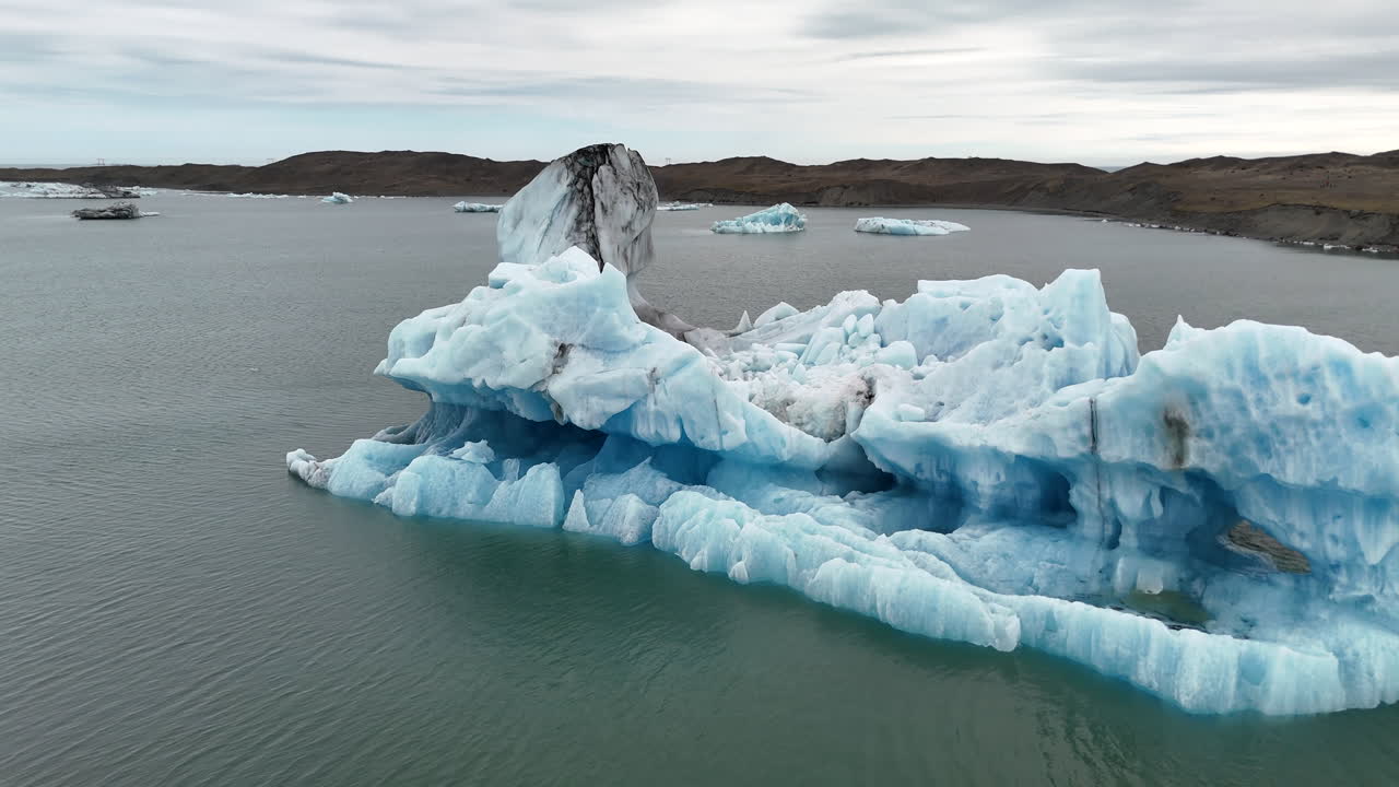 Aerial view of a massive iceberg floating in Jökulsárlón Glacier Lagoon, Iceland, highlighting the icy blue waters, surrounding glaciers, and serene Arctic scenery