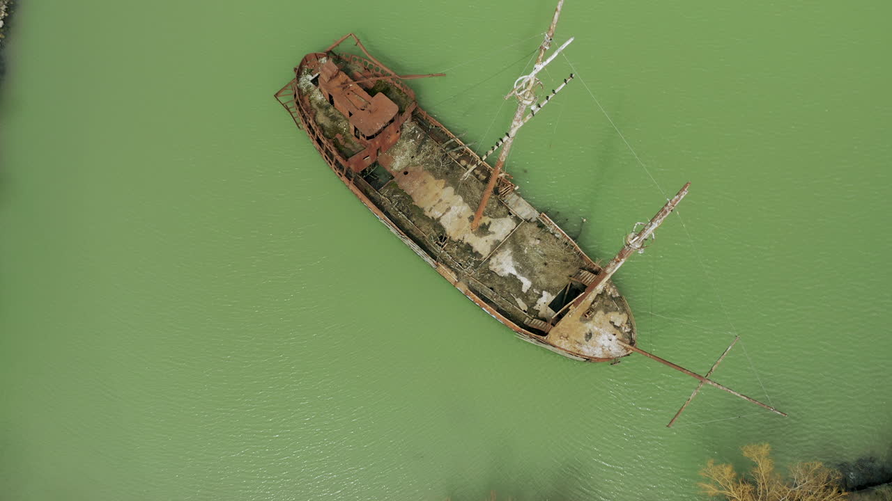 Rusty red shipwreck stuck in shallow green water