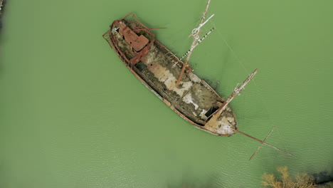 rusty red shipwreck stuck in shallow green water