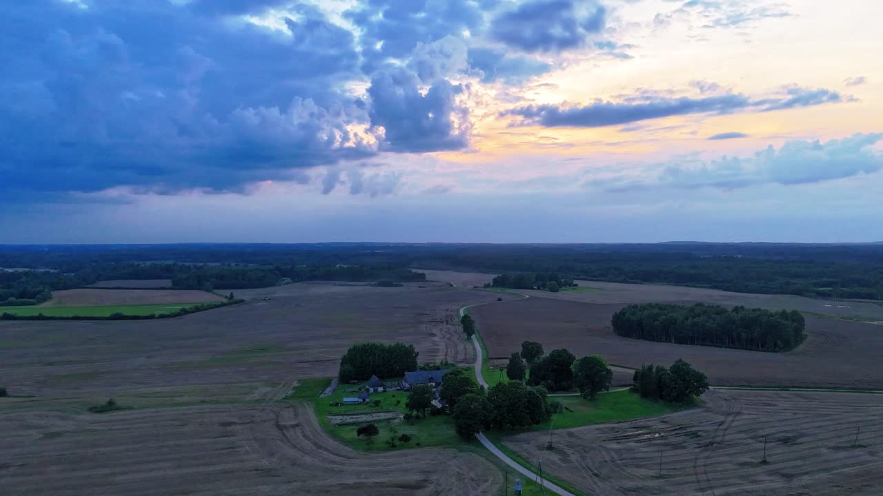 Timelapse Drone Shote of Sunset Harvest in Latvia Combines Collecting Rapeseed Surrounded by Vast Agricultural Fields and Dramatic Clouds in the Sky the Rhythm of Rural Life in Golden Light