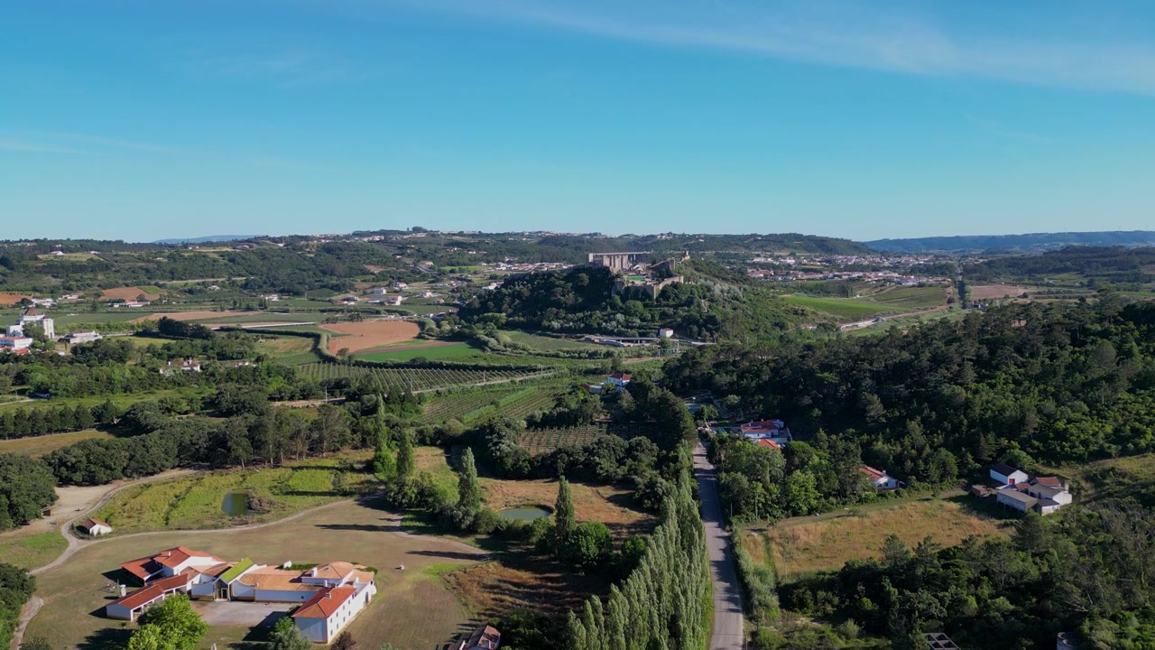 Vista aerea del Castello medievale di Óbidos in Portogallo, circondato da affascinanti case imbiancate a calce e strade acciottolate. Il paesaggio soleggiato mette in risalto le dolci colline verdi e la storica città sottostante