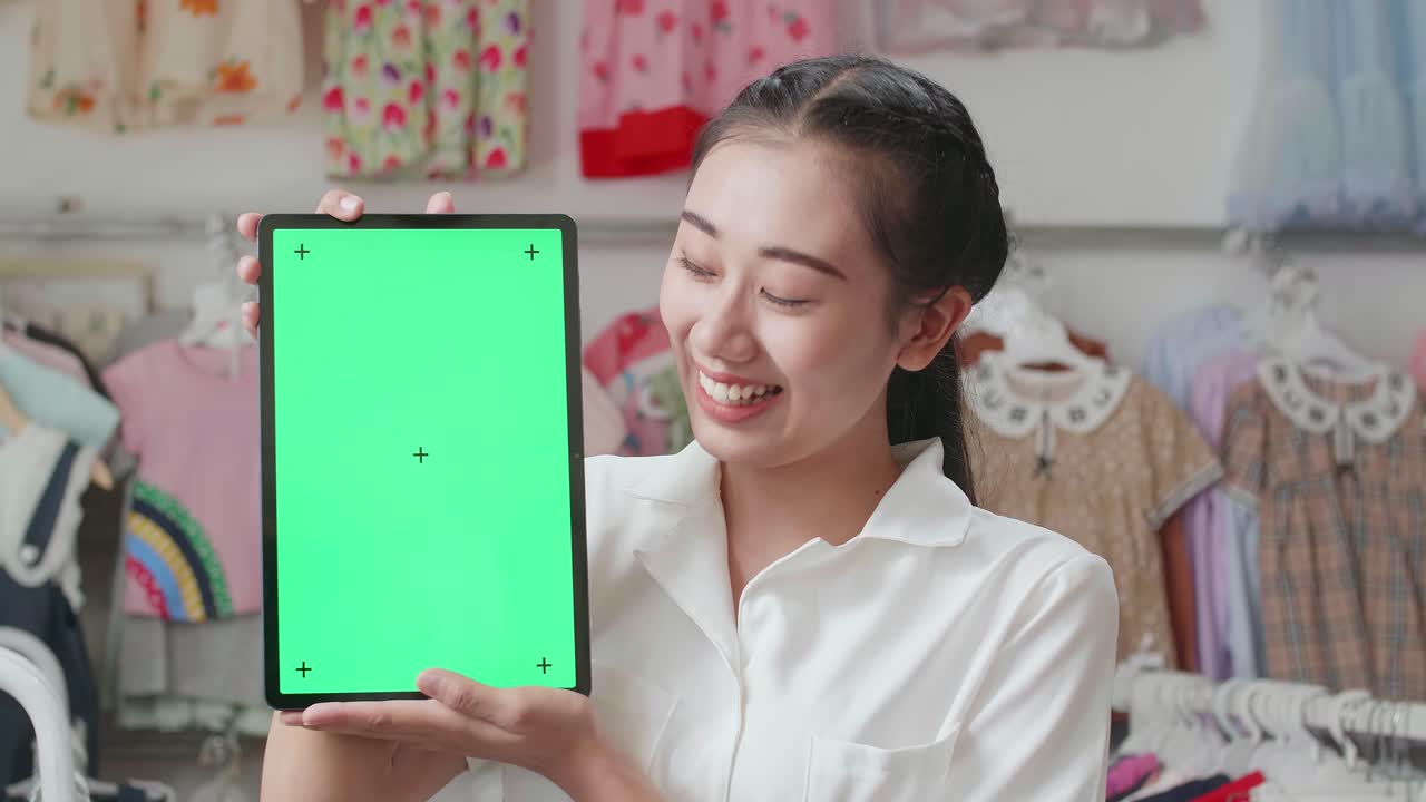 부티크에서 쇼핑하는 동안 카메라에 녹색 화면 태블릿을 보여주고 미소 짓는 아시아 어머니의 클로즈업