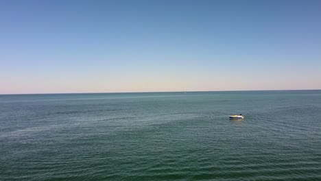 aerial flyover calm ocean with small boat enjoying watersports