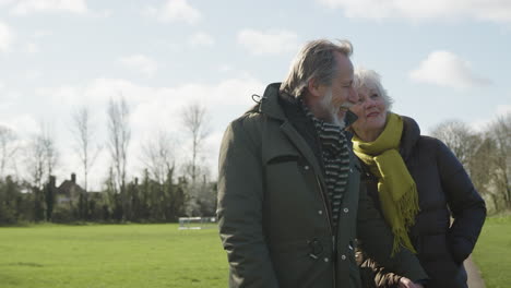 Loving-Senior-Couple-Enjoying-Autumn-Or-Winter-Walk-Through-Park-Together