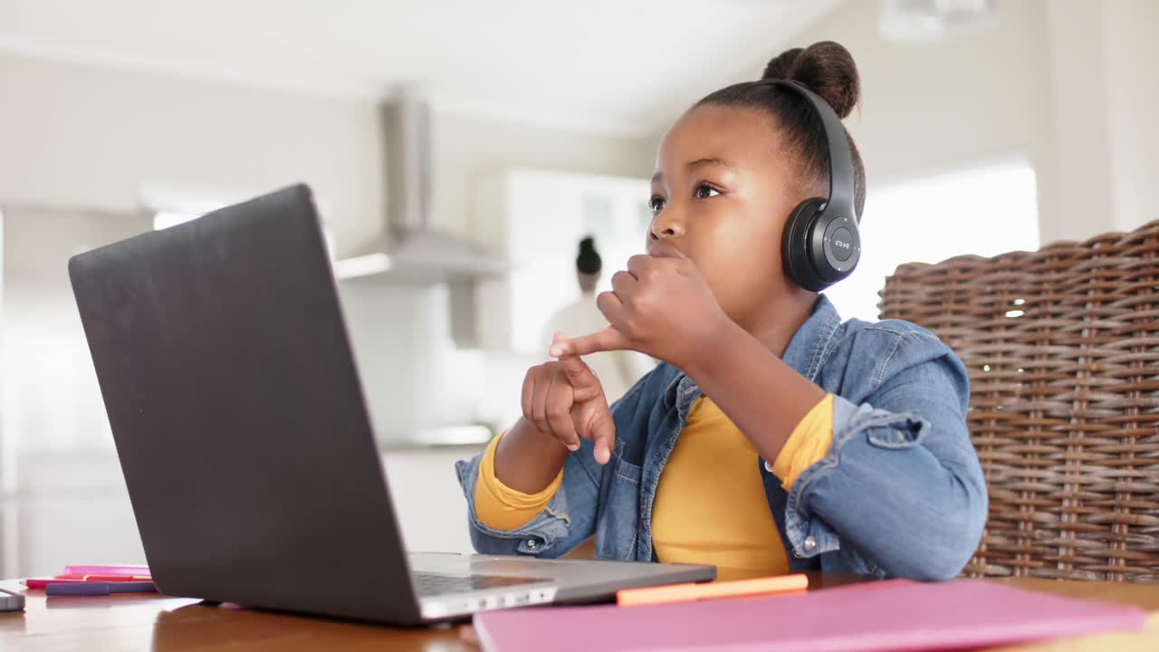 Happy unaltered african american girl using laptop and headphones for online lesson, in slow motion