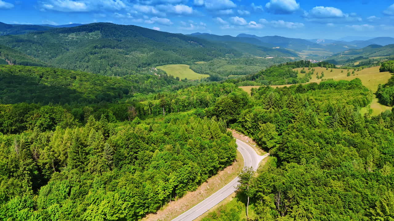Winding road in green hills. A winding road cuts through vibrant green forests and hills under a clear blue sky in a sunny landscape