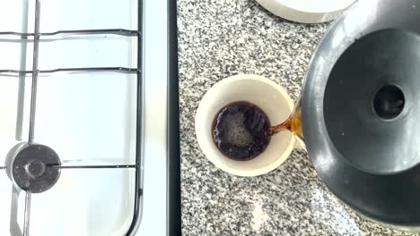 view from above, pouring coffee from a coffee pot into a cup near a gas stove