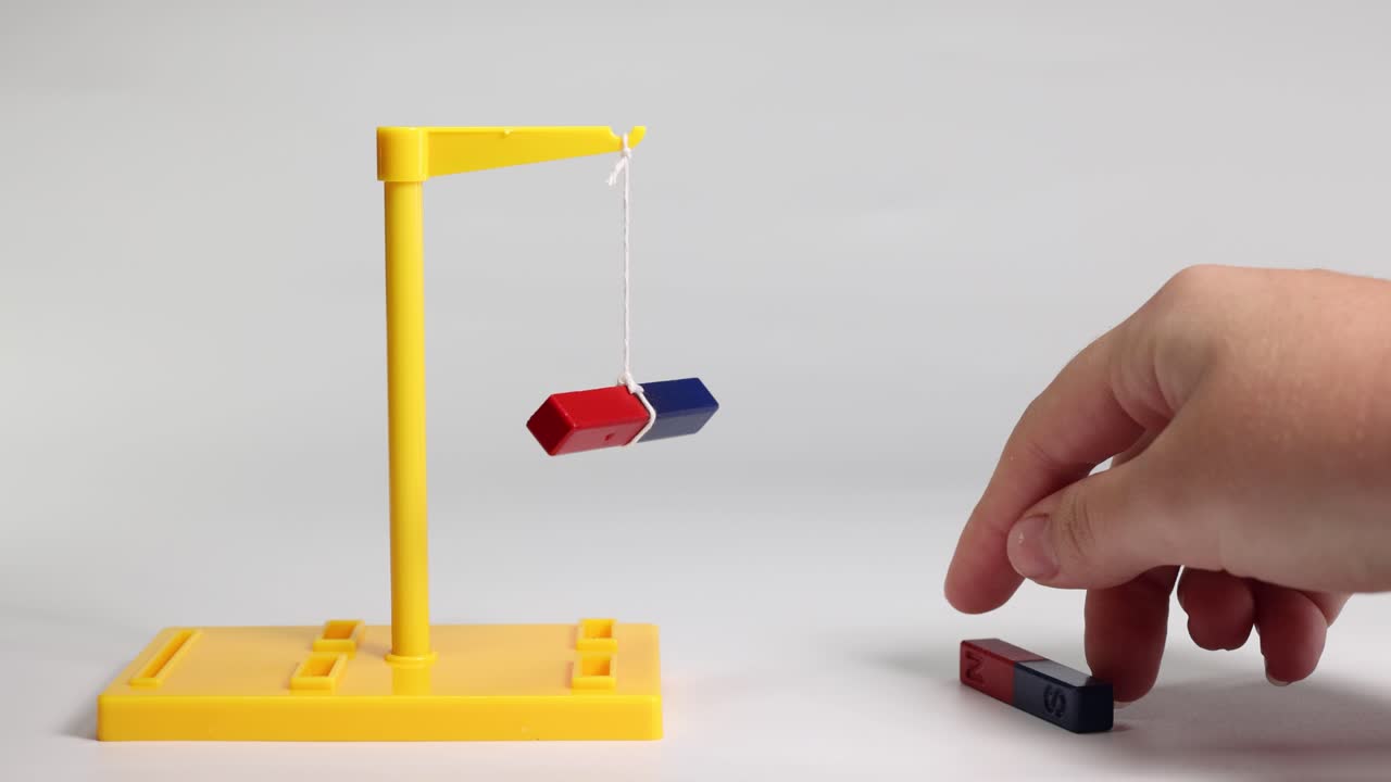A suspended magnet interacts with a handheld magnet, illustrating attraction and repulsion in a controlled environment
