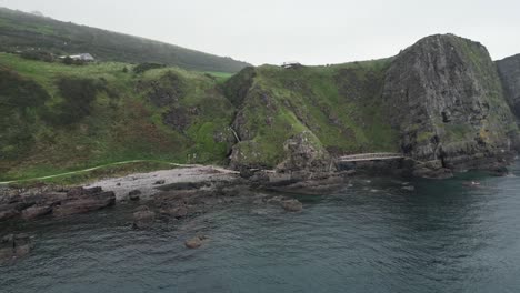 Aerial-dolly-shot-of-the-Gobbins-Cliffs-in-Northern-Ireland-during-an-adventurous-journey-overlooking-the-coast-road,-calm-sea-and-rocks-on-a-cloudy-morning-on-an-expedition