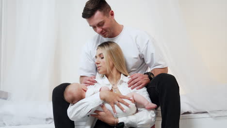 beautiful woman waving her baby in hands. man sits above his wife kissing her on the head.