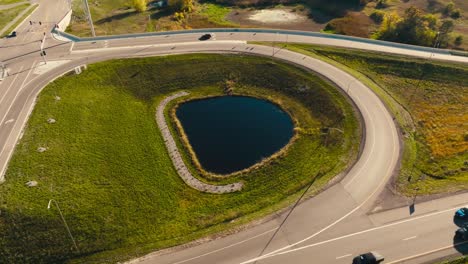 disparo aéreo de un avión no tripulado de una entrada de paso elevado de autopista y rampa de salida con un pequeño estanque en el medio con coches moviéndose en la autopista en un día soleado