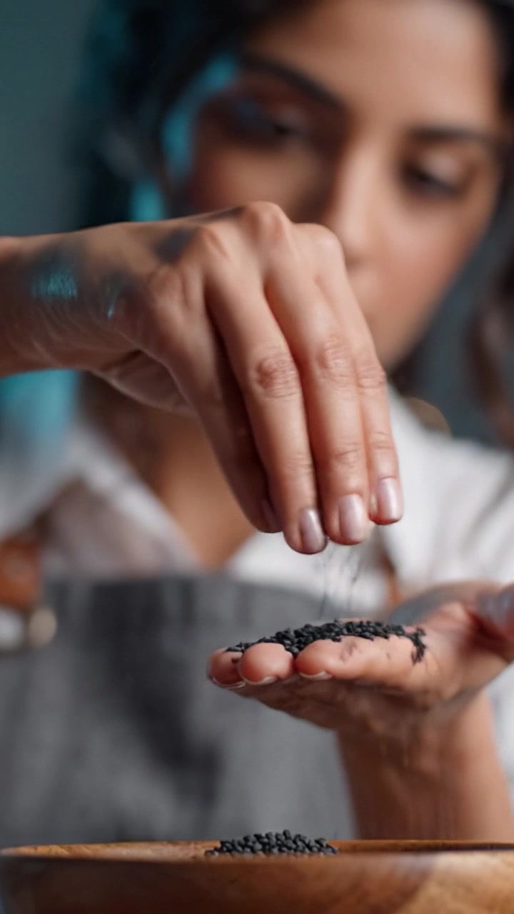 Un primo piano di una persona che maneggia con cura semi neri in una ciotola, con un focus su texture e dettagli in un ambiente culinario intimo.
