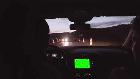 man driving modern sports car on a highway with road under construction in evening time using navigation on his smart phone with blank green screen