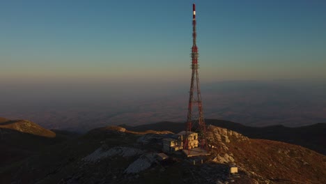 aerial approaching large telecommunications tower on a mountain peak at sunrise