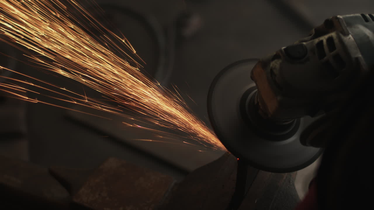 las chispas vuelan en círculo mientras la amoladora angular bisela el borde del metal en el banco del taller.