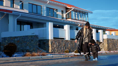 modern caucasian mother walks holding her son by the hand. mom and baby in sunglasses outdoors on sunny winter day.