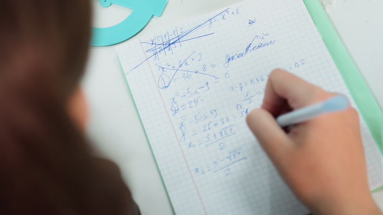 estudiante escribiendo notas en papel cuadriculado, primer plano de una mano femenina sosteniendo un bolígrafo azul junto a una carpeta color menta, resolviendo ecuaciones en un cuaderno cuadriculado, escena de escritorio tranquila, concentración durante la preparación del examen