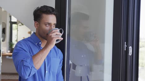 Fröhlicher-Gemischtrassiger-Mann,-Der-Kaffee-Trinkt-Und-Aus-Dem-Fenster-Schaut,-Zeitlupe