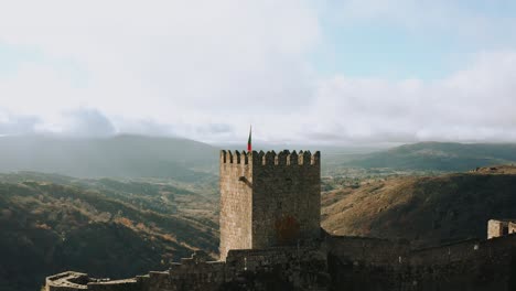 Medieval-historical-castle-turret-with-flag-overlooking-deep-canyon,-aerial-dolly-in