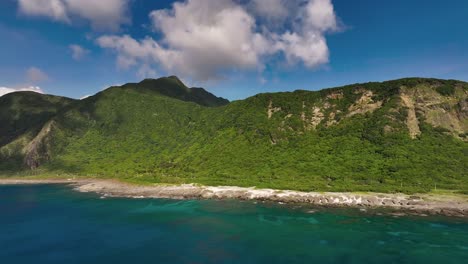 Aerial-approaching-shot-of-green-Orchid-Island-with-coastline-and-blue-ocean-during-sunny-day