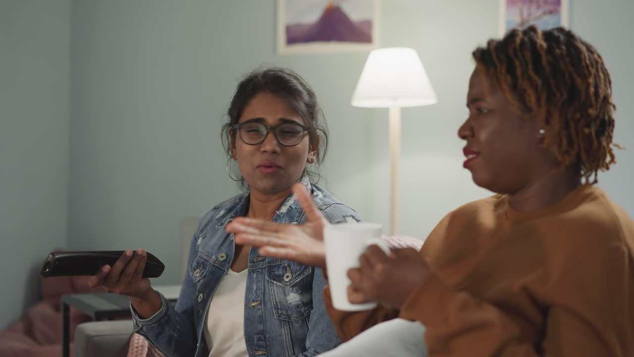 la mujer bebe té mientras el amigo cambia de canal con control.