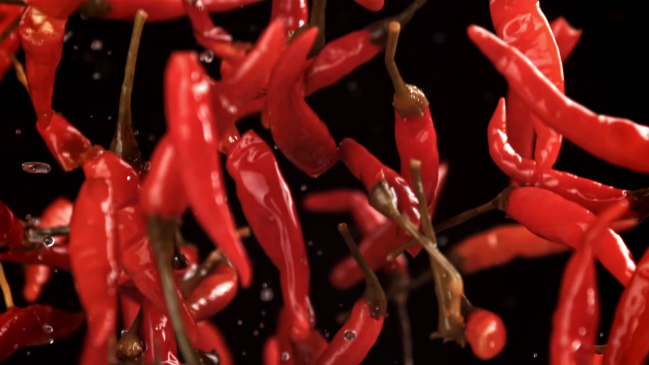 Vibrant Red Chili Peppers Falling with Water Splashes on Black