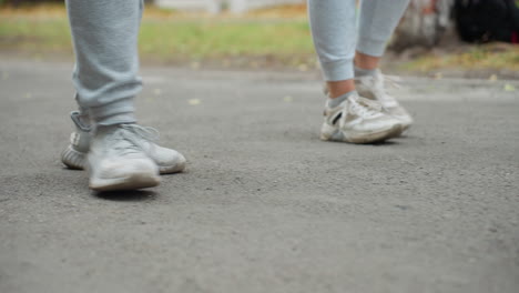 lower angle view of two individuals walking side by side in grey joggers and sneakers, captured mid-step on paved road with greenery in blurred background