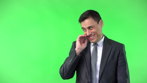 A man in a suit laughing and scratching his neck on a green screen